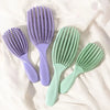 A set of four purple and green massage detangler hair brushes lying on a white surface.