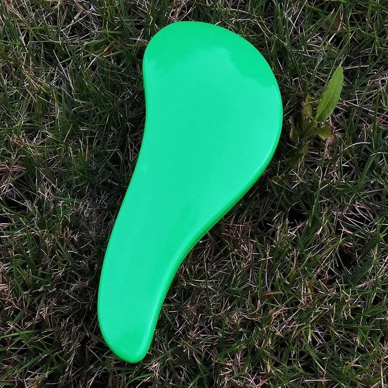 A bright green classic detangling hair brush lying on green grass.