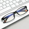 A pair of black-framed reading glasses with blue and orange accents resting on a white background next to a silver keyboard.