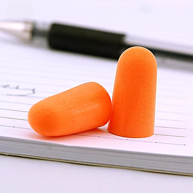 Gros plan de bouchons d'oreille anti-bruit orange vif posés sur du papier et un stylo.