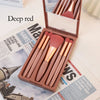A set of ten professional makeup brushes in a deep red or rose gold color displayed in an open wooden box.