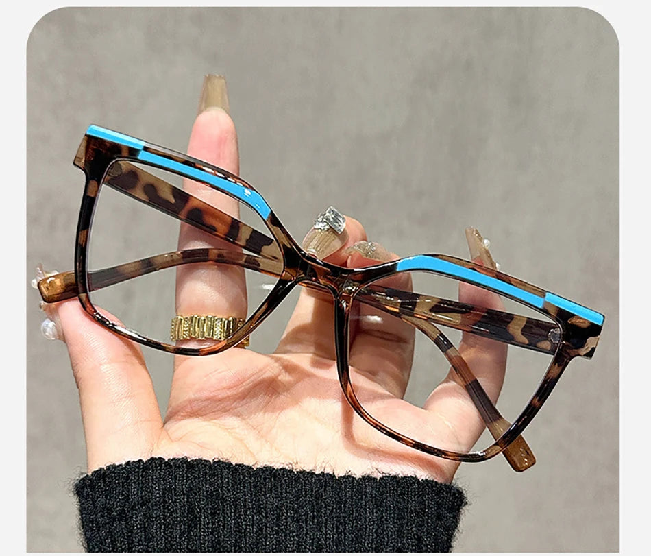 Una mano sostiene unas gafas de lectura marrones tortugas con detalles azules contra un fondo gris.