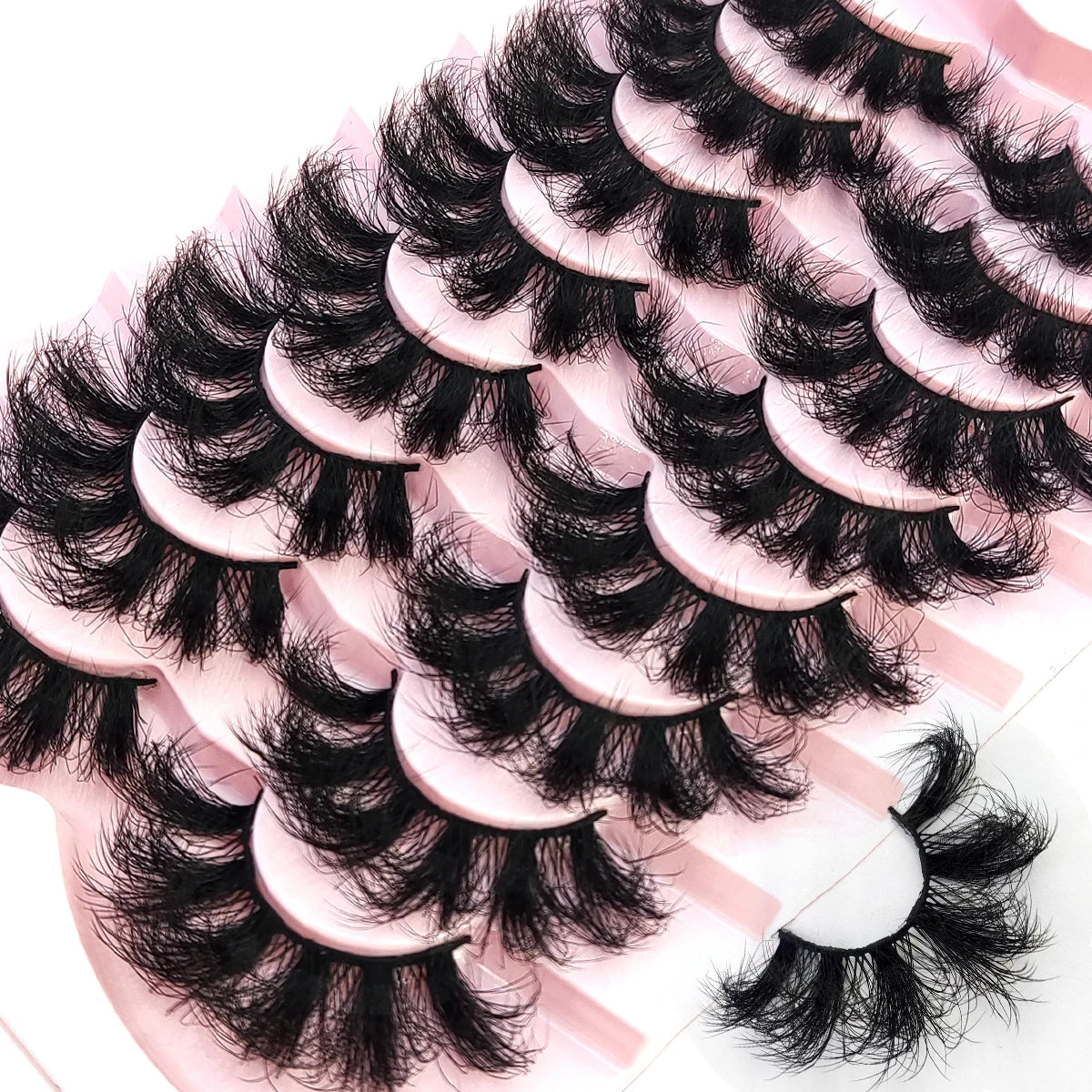A close-up of natural mink striped false eyelash extensions arranged on a pink surface.