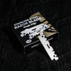 A box containing a single stainless steel razor blade is displayed on a dark wooden surface.