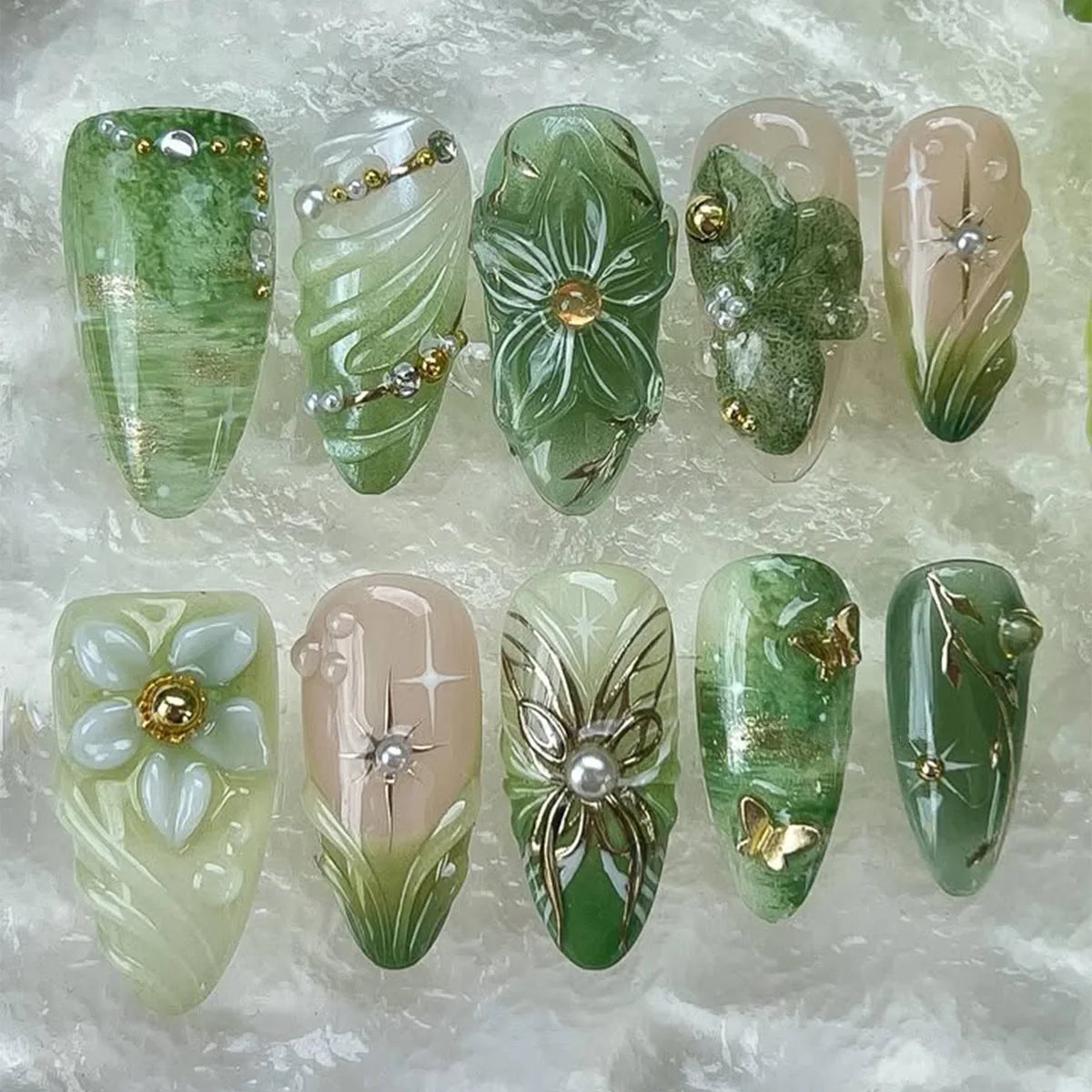A collection of 24 press-on almond nails featuring various shades of green and natural floral and butterfly designs.