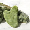 A smooth, light green jade gua sha tool rests on a white marble surface.