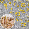 Gold hibiscus flower nail decals applied to a natural pink nail, shown on a gray background.