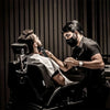 A man is receiving a haircut or grooming service from a professional using an electric hair clipper trimmer kit.