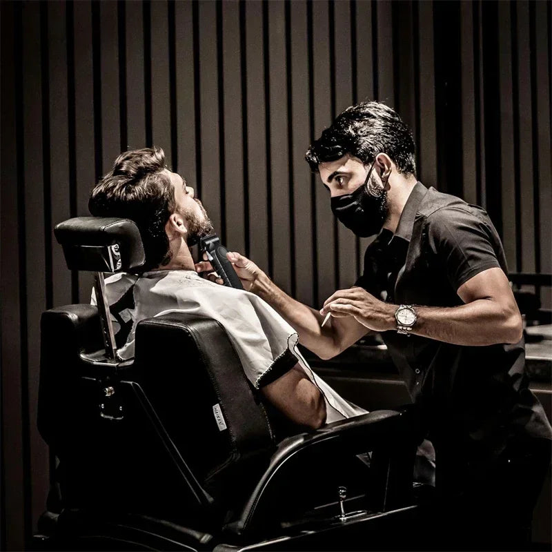 A man is receiving a haircut or grooming service from a professional using an electric hair clipper trimmer kit.