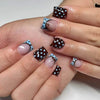 A close-up of a hand displaying reusable press-on nails with a pink base and dark brown polka dots and fine lines.