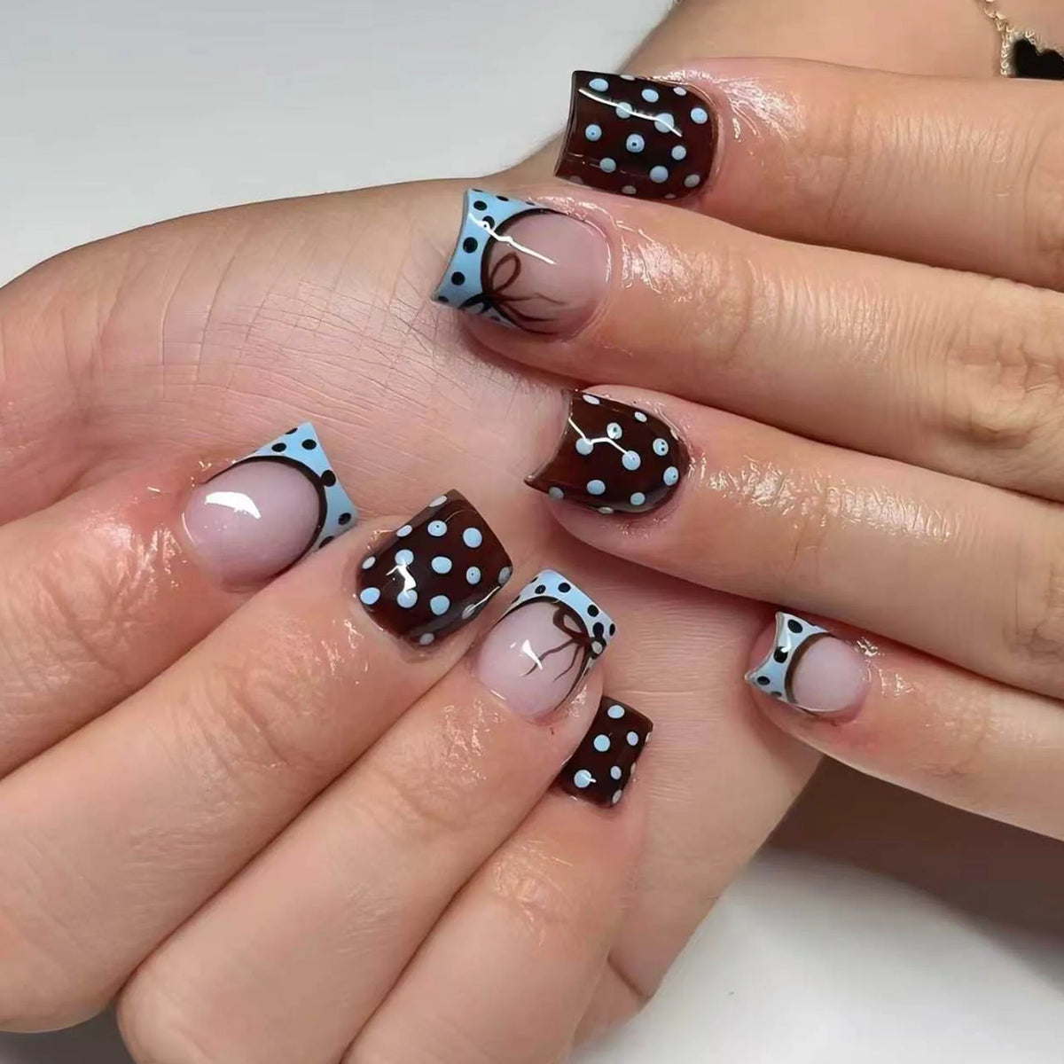 A close-up of a hand displaying reusable press-on nails with a pink base and dark brown polka dots and fine lines.