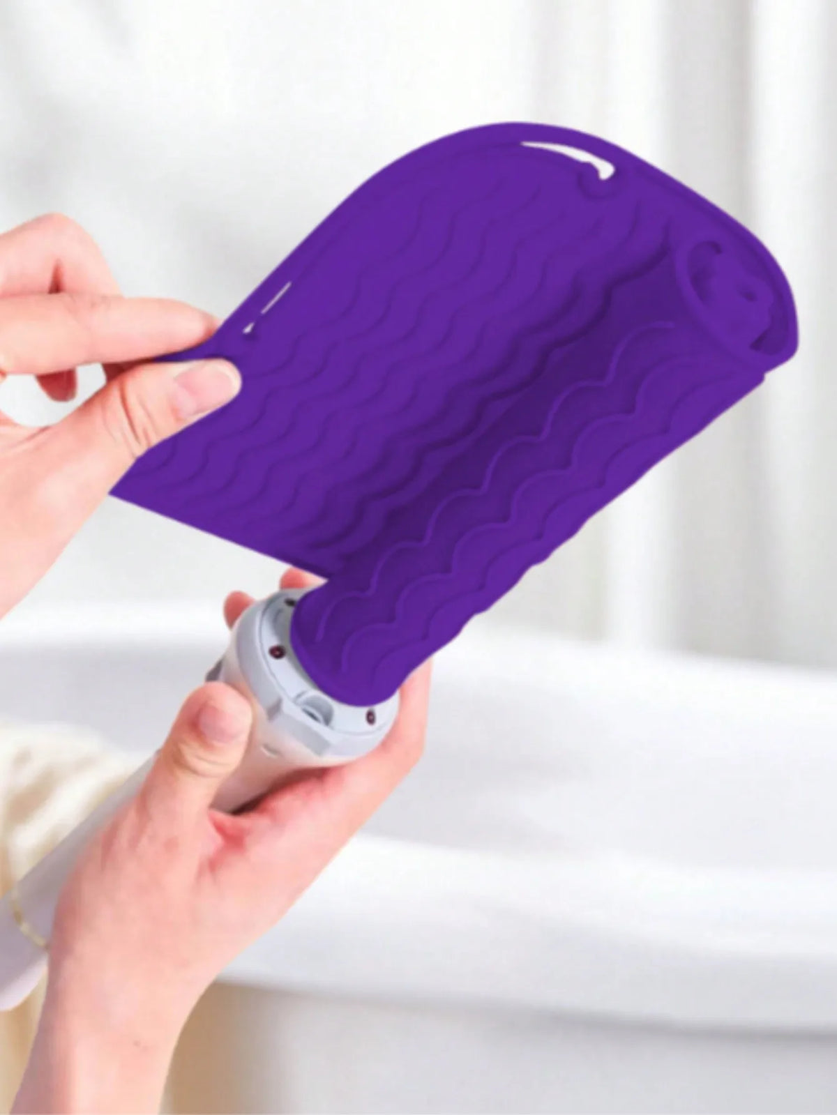 A hand is holding a purple silicone heat resistant mat for hair styling tools.
