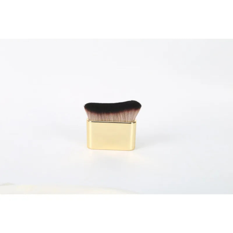 A gold-colored makeup brush with dark bristles for tan and foundation application.
