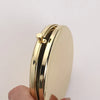 A gold-colored portable folding makeup mirror with a magnifying feature is held in a hand.