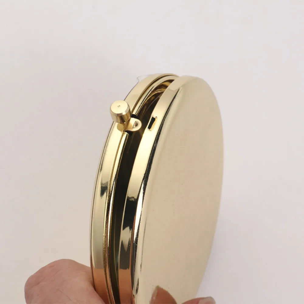 A gold-colored portable folding makeup mirror with a magnifying feature is held in a hand.