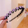 A hand holds a black rhinestone wave headband with purple flowers against a light background.