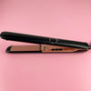 A black ceramic flat iron hair straightener with a rose gold finish resting on a pink background.