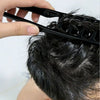 A hand is using a black hair styling comb set to style dark hair on a person's head.