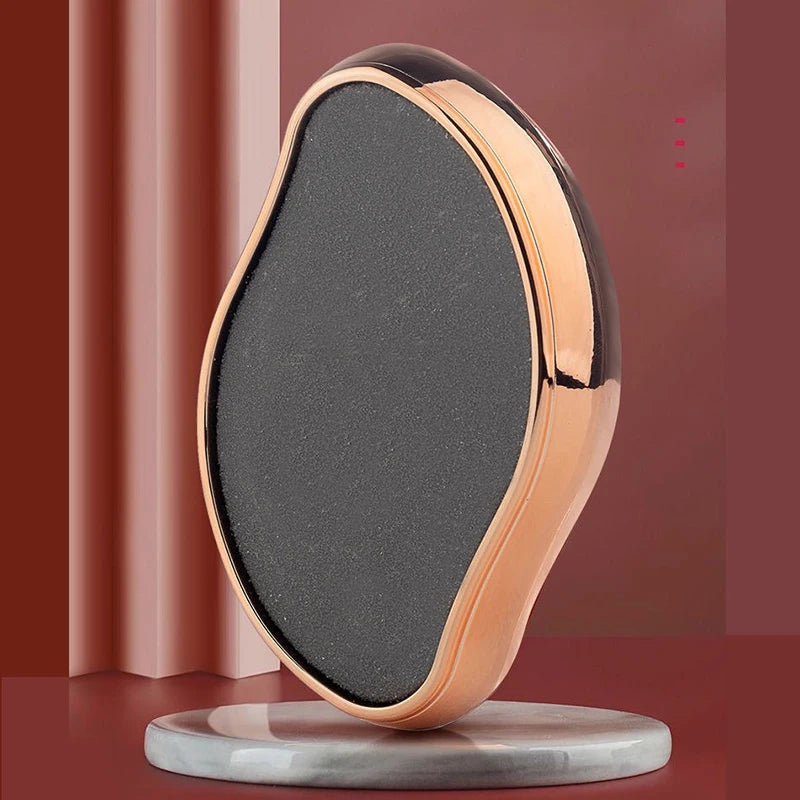 A portable glass foot file and callus remover tool with a smooth, oval shape and rose gold finish resting on a gray base.