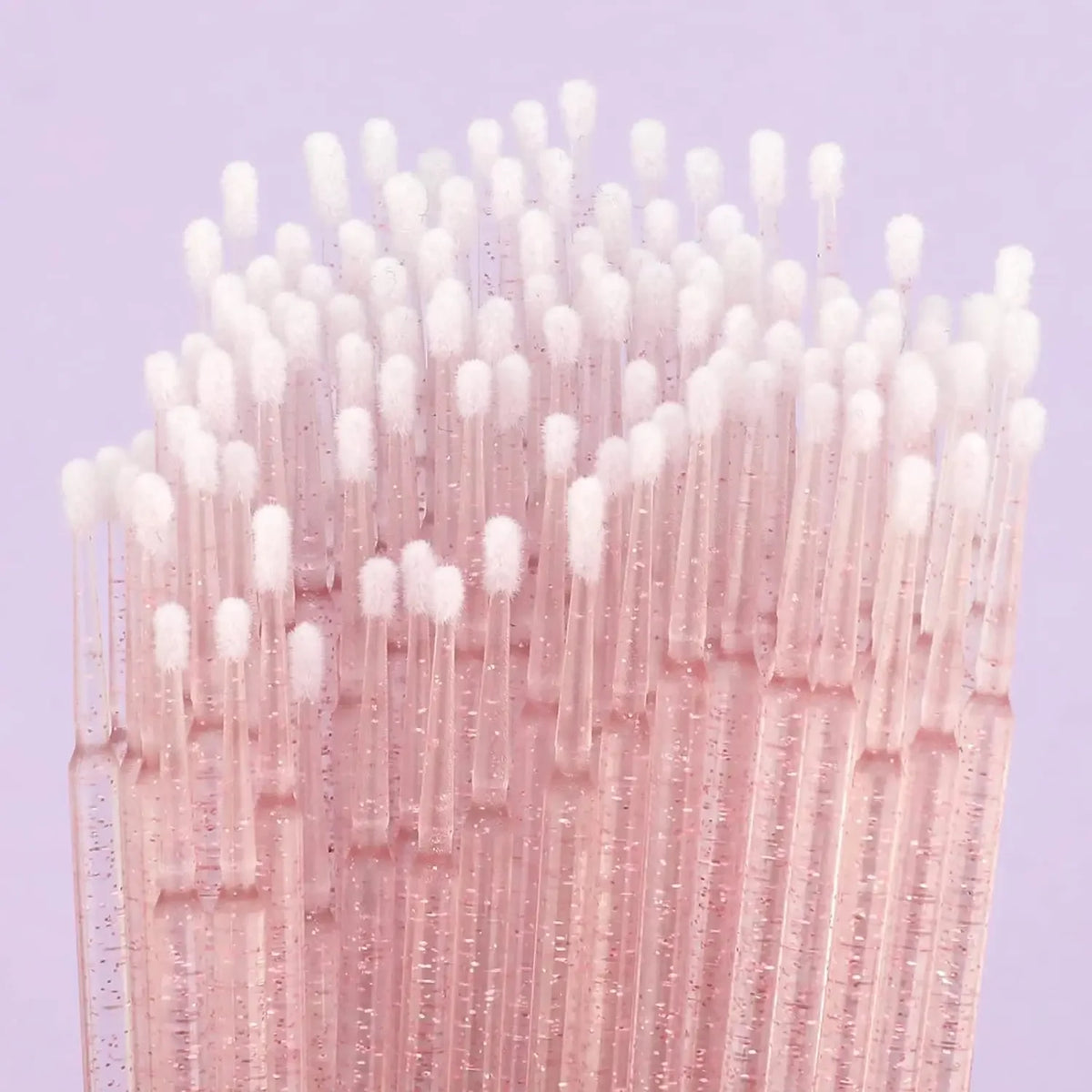 Gros plan d'un ensemble de micro-pinceaux d'application en cristal rose transparent avec de fines poils synthétiques.