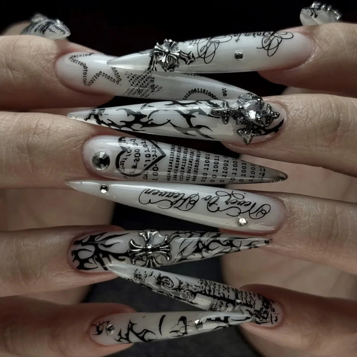 Gros plan de doigts montrant divers kits de vernis press-on en forme de fleur d'amande avec des motifs noir et blanc.