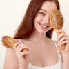 A woman is holding a natural bamboo hair brush, demonstrating its use for detangling or scalp massage.