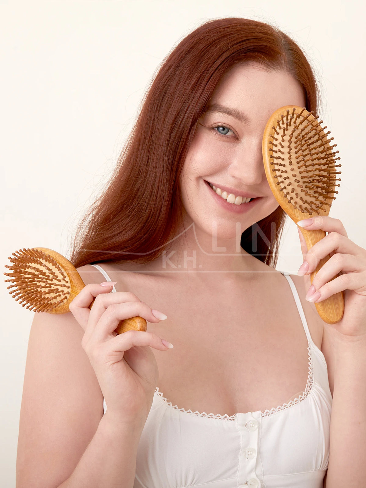 A woman is holding a natural bamboo hair brush, demonstrating its use for detangling or scalp massage.