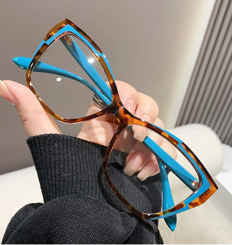 A hand holds a pair of orange-tinted cat eye reading glasses with bright blue frames against a dark sweater.