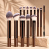 Un set de brochas de maquillaje profesionales de doble punta con mangos de madera oscura y cerdas esponjosas, de pie.