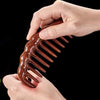 A hand holds a brown natural golden sandalwood wide-tooth detangling comb against a black background.