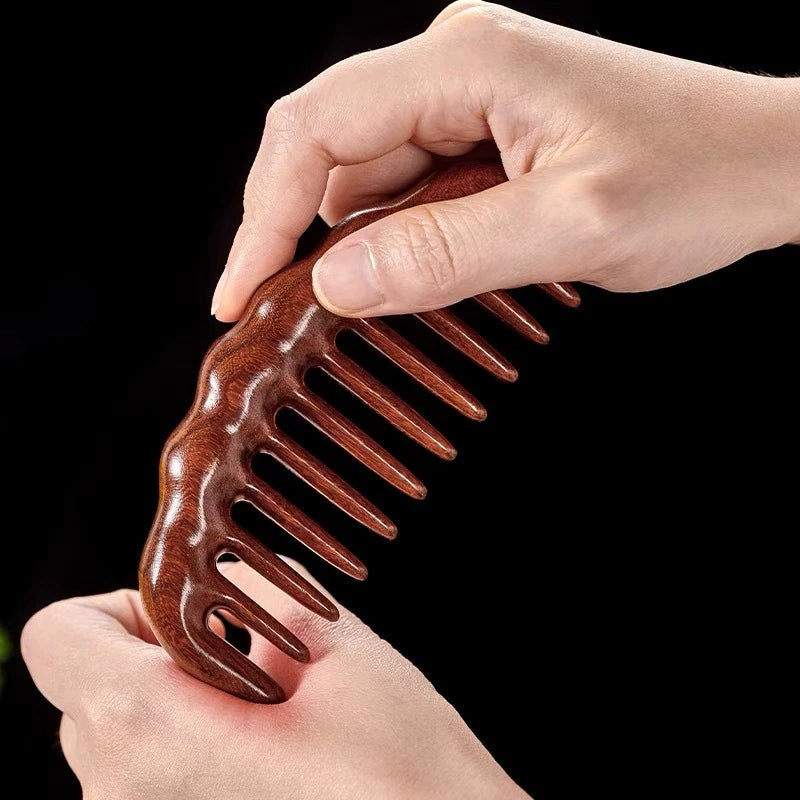 A hand holds a brown natural golden sandalwood wide-tooth detangling comb against a black background.