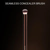 Un pinceau de correcteur sans couture Hourglass long et fin, de teinte rose gold, est exposé sur un fond sombre.