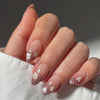 Close-up of a hand displaying press-on acrylic nails decorated with small white and gold flowers.