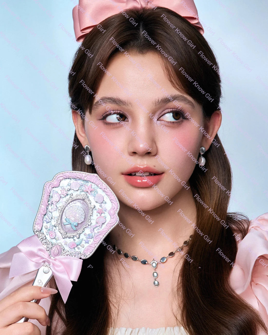 A young woman holds a pearl hand mirror for makeup and beauty, featuring a pink bow.