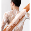 A person's back is shown with a white exfoliating sponge covered in brown scrub particles.