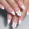 A hand displays nude pink press-on nails decorated with white hearts and floral charms.