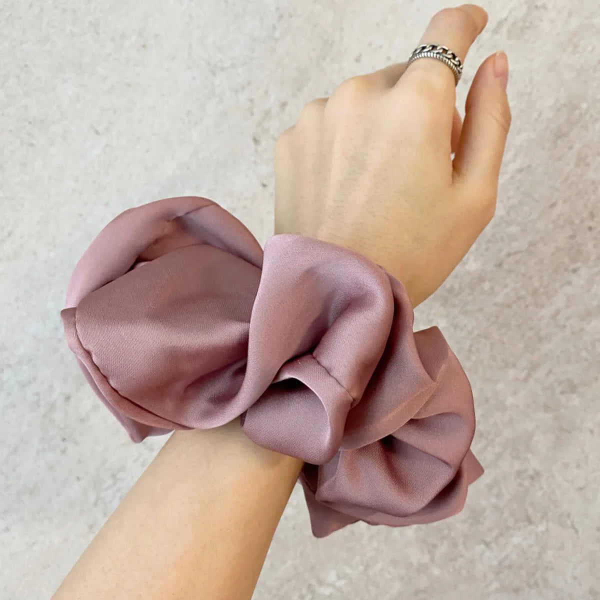 Une main portant un bracelet en mousseline de satin rose poudré noué en nœud.