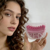 A woman holds a pink natural rubber gua sha tool for face and neck massage.