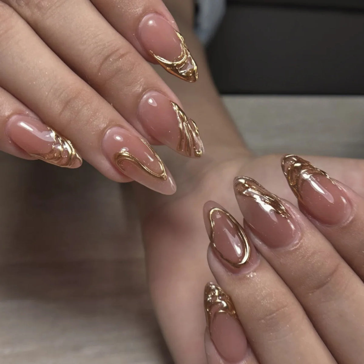 Close-up of a hand displaying pink flower almond press on nails with gold metallic accents.