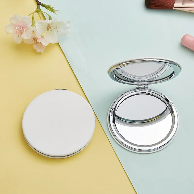 A portable magnifying makeup mirror with a silver frame and round mirror is shown on a light green surface.