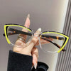 A hand holds a pair of yellow-framed cat eye reading glasses with brown lenses against a light background.