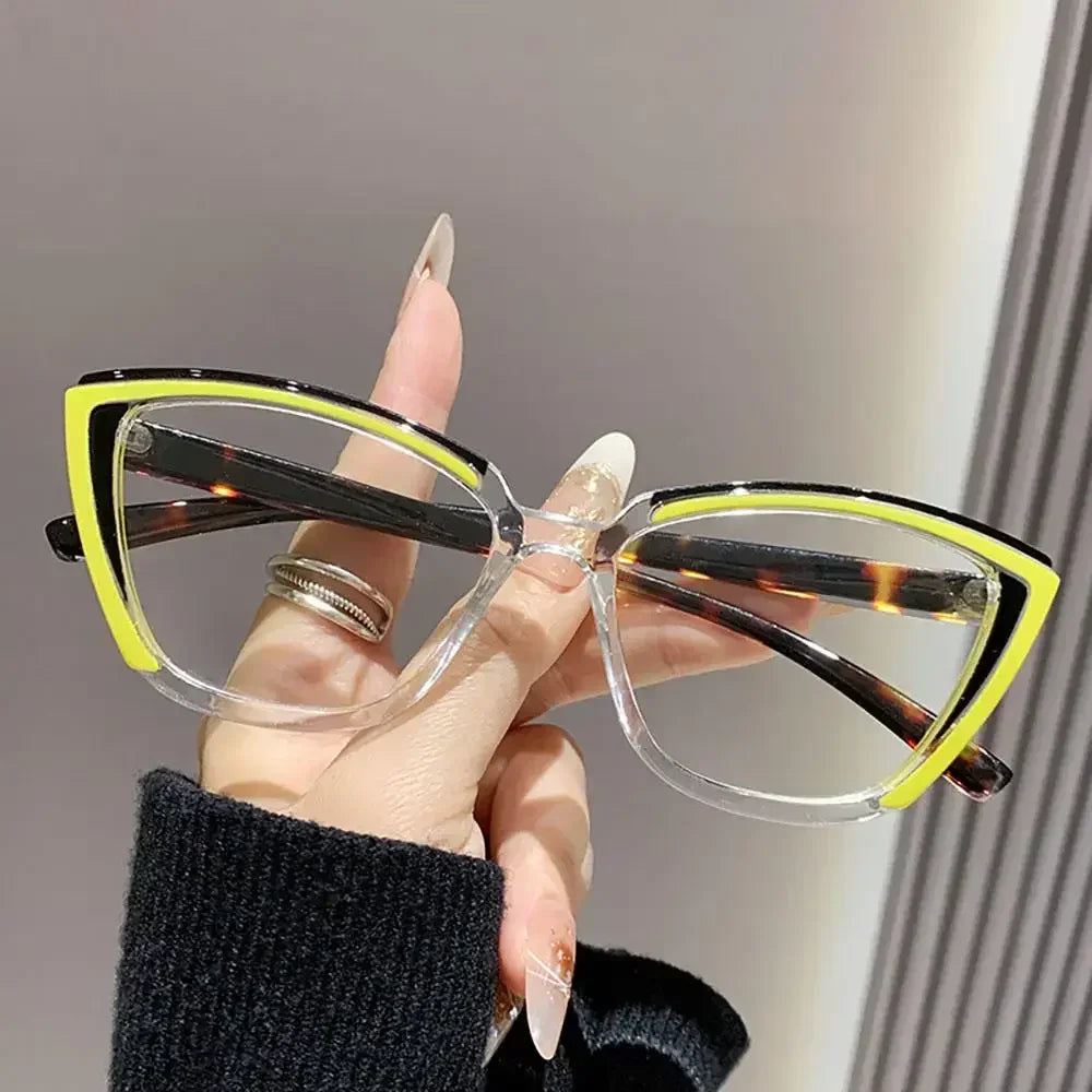 A hand holds a pair of yellow-framed cat eye reading glasses with brown lenses against a light background.