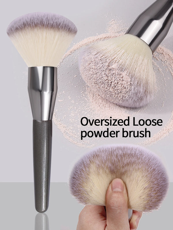 A silver oversized loose powder brush with soft purple and beige bristles shown next to a hand.