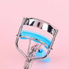 A stainless steel eyelash curler with a precision comb is shown against a pink background.