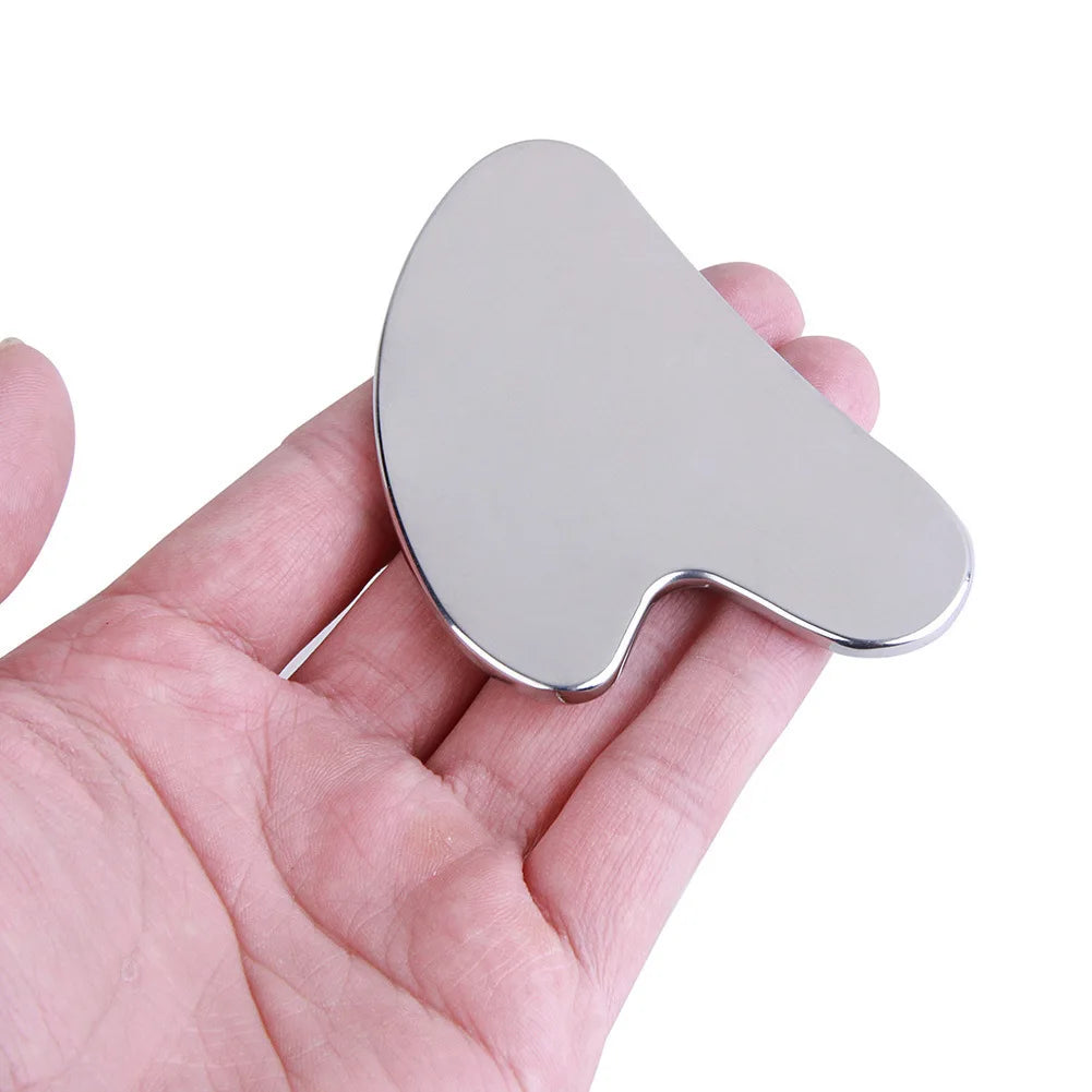 A hand holds a smooth, oval-shaped stainless steel gua sha tool for facial and body massage.