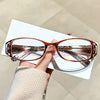 A hand holds a pair of thin, orange-tinted reading glasses with reflective lenses against a white background.