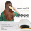 A woman is using a natural boar bristle hair brush with a bamboo handle to style her long brown hair.