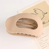 A beige oval flat hair clip is shown resting on a piece of paper with a line drawing of a bird.
