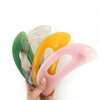 Une main tient un jeu de cinq outils de massage Guasha en pierre naturelle aux tons vert, beige, orange et rose.