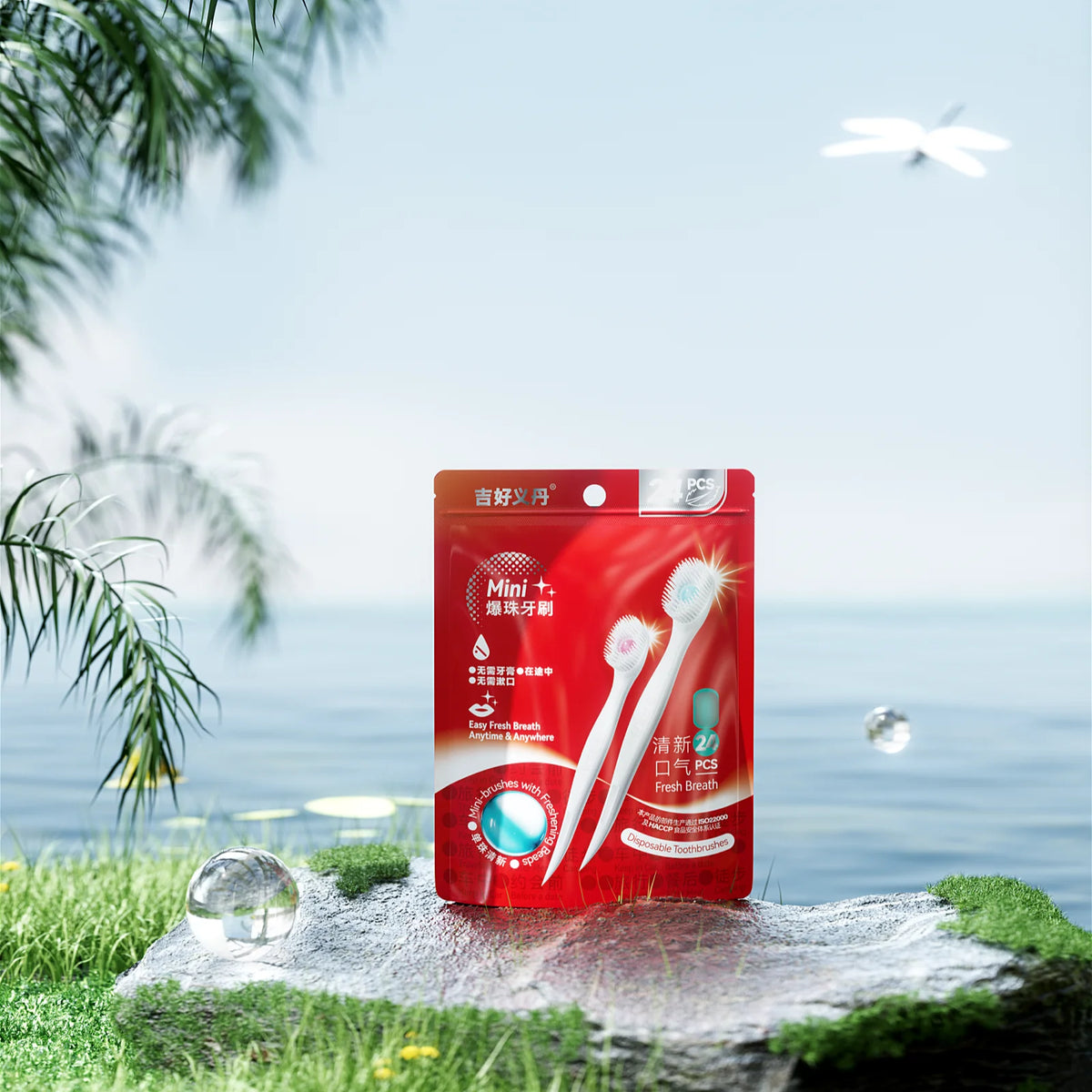 A red box of a 24-piece portable toothbrush set is displayed on green grass near the ocean with a bird flying above.